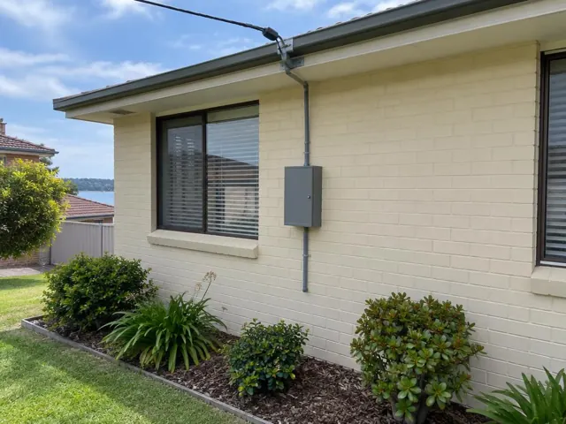 Cream brick house exterior with overhead service cable and point-of-attachment bracket on the wall in Speers Point