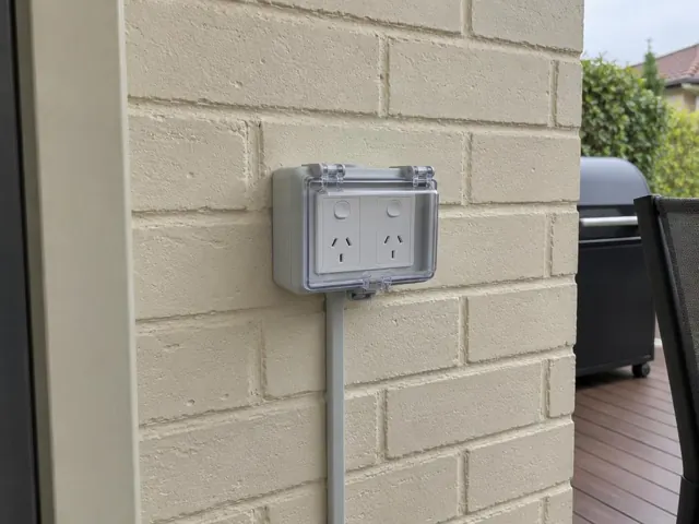 Outdoor double power point on a painted brick exterior wall beside a deck in Glendale